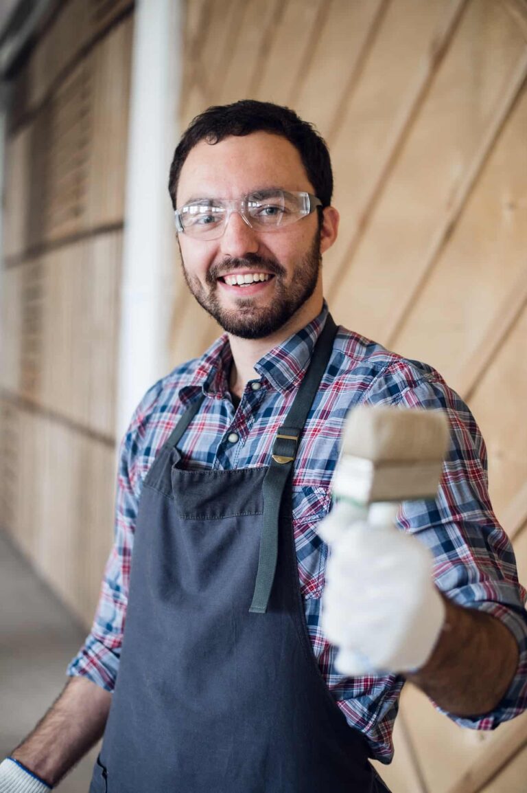 happy-young-painter-holding-paint-brush-and-showing-it-to-camera